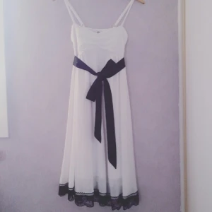  - Romantisk vit klänning i lätt yttertyg (underkjol något krafigare - ej genomskinlig). Svart sidenband om midjan som enkelt plockas bort om en vill det. Vacker svart spets i nederkant.  Använd en gång. 