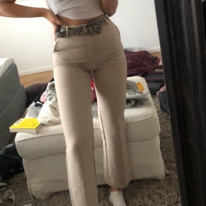 Beiga Kostymbyxor - Beiga kostymbyxor från Gina Tricot i storlek 34. Dessa sitter super fint på och är medelhöga. De är sitter lite tightare över låten och raka nertill. Lite croppad modell