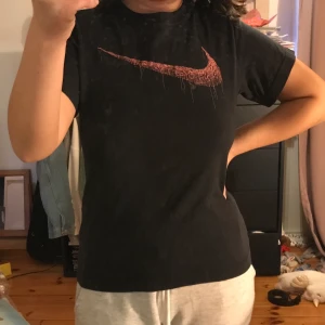 Svart Nike T-shirt  - BUDGIVNING PÅ DENNA. Höj med minst 10kr. Startpris 70kr. Avslutas söndag 22/11 En svart Nike tröja med rosa logga. Storlek S men skulle säga att den sitter mer som en XS. Endast använd ett fåtal gånger och i fint skick. Kan mötas upp i Eskilstuna eller frakta (frakten ligger på 59kr). Tvättas innan den skickas.