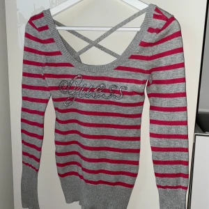 Randig Guess tröja i storlek XS - Rosa/grå randig tröja med korsade band i ryggen & Guess skrivit med glitter på bröstet. Köpt i New york på Guess i storlek xs! Frakt ingår!