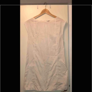  - Somrig vit klänning i ”skjort-material”. Tunn, lätt, skön, hänger rakt på kroppen. 