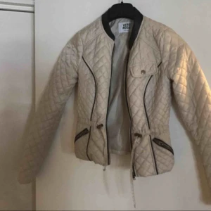  - Beige jacka som man kan dra åt i midjan. 34