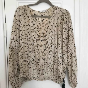  - Fin blus i ett snyggt mönster med beiga toner.  Finns en dragsko så man kan dra åt den längst ned.  Jättefint till sommaren! 