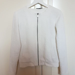 Vit tröja med mönster - Vit och typ inte använd tröja med dragkedja och två fickor, rätt mys och passar till det mesta. Har ett lite "utstående" blommönster. Frakt ingår!