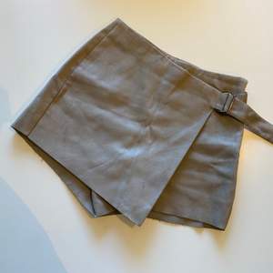 Supersnygga beige/gråa shorts i mockatyg. De ser ut som en kjol framifrån men är shorts bakifrån. Spänne i midjan som kan reglera storleken. 