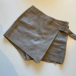 Kjol/shorts - Supersnygga beige/gråa shorts i mockatyg. De ser ut som en kjol framifrån men är shorts bakifrån. Spänne i midjan som kan reglera storleken. 