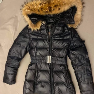 Hollies dunjacka strl 36 - Svart Hollies dunjacka i storlek 36.   Avtagbart bälte i midjan, stor, härlig luva med krage i äkta päls (mycket välvårdad)  Jackan finns i Alingsås, kan även skickas per post, vilket i så fall kostar 88 kronor. Postar samma dag som betalningen finns på kontot :) 