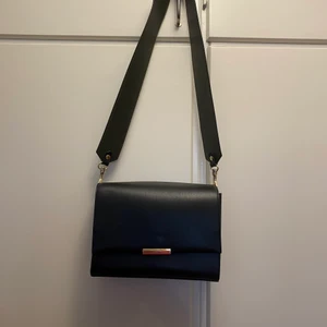 & other stories väska ”Duo Tone Leather Crossbody” - Inköpt julen 2019 för ca 1750 kr, kvitto finns. En väska i skinn i färgensvart med gröna detaljer, fodret innuti är i bomull. Väskan är i gott använt skick då den endast användes 15-20 ggr. 25 x18 cm. Säljer pga inte min stil längre.