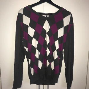 Stickad tröja - Svart/mörkgrå stickad tröja med vita och lila rutor. Aldrig använd, i storlek L (skulle säga att den passar M/är mer som en M) inga fläckar eller hål mm. Köparen står för frakten