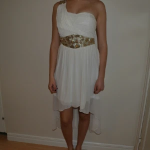  - Vit chiffongklänning i high to low modell, 
gudliga paljett/glitter detaljer i midja och på axel.
Storlek 38, men passar även på mig som vanligtvis är 36. 
Använd en gång, nyskick!