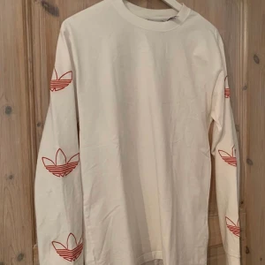 Adidas tröja - Som en tröja i t shirt material men långärmad med röda adidas märken tryckta på ärmarna