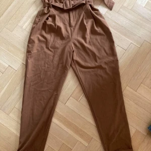 Paper bag bruna byxor Bershka, strl 36. - Säljer ett par bruna paperbag byxor från Bershka. Köpta för två år sen, men har inte använts på ett år. Byxorna är högmidjade men lite kortare i längden på mig som är 168 cm. Säljer för 100 kr och köparen står för frakt (65kr). 
