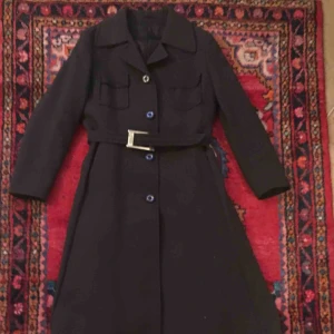  - Väl omhändertagen figursydd,  äldre svart kappa med fickor, och skärp i midjan. Stängs med knappar. Köpt på vintage butik. Aldrig använd av mig, bara testad hemma, står 42 i len skulle säga att den passar M/L. 