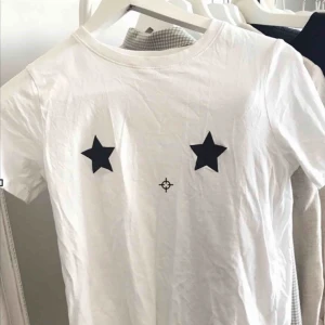  - Vit T-shirt med stjärnor över brösten.