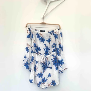  - Vit off-shoulder playsuit med blåa blommor i mycket bra skick. Är i storlek 38 men passar mer en 36. Fraktar eller möts upp i Stockholm (köparen står för frakten).