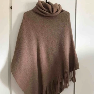  - Brun poncho med stor krage och fransar nertill. Använd en enstaka gång och därmed i väldigt fint skick.  Köparen står för frakten. Kan även mötas upp i Karlskrona.