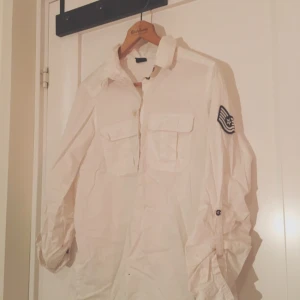  - Vit, ganska lång skjorta i ett ganska tjockt material. Har ett emblem på ena ärmen. Från Gina tricot