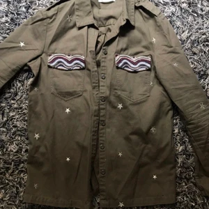 Grön jacka med broderade stjärnor  - Superfin militärgrön jacka med broderade stjärnor och andra snygga detaljer. Köpt i Spanien och använd endast fåtal gånger, bra skick! Storlek L men passar mig som brukar ha small-medium