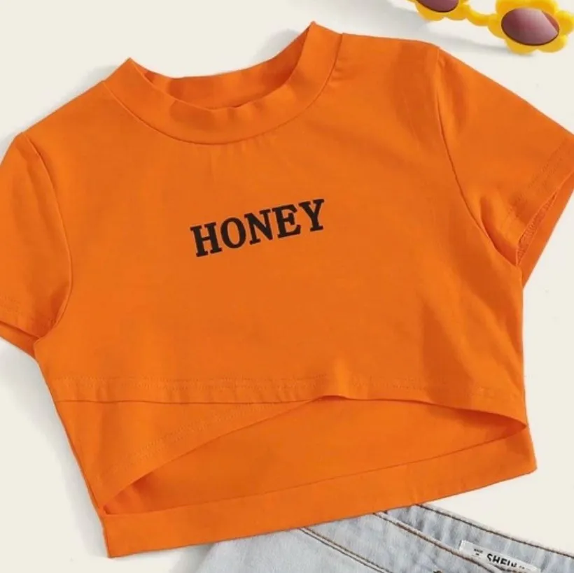 An orange crop top. In the middle it says honey . Toppar.