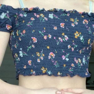 Croppad mörkblå topp - Kort tröja med blommmönster från bikbok. Aldrig använd. Däremot insydd i ärmar då den var väldigt stor vid axlarna men det är extremt strechigt material så den pssar på en xxs-s (beroende på hur kort man vill ha den)💖.                                               Köparen står flr frakt