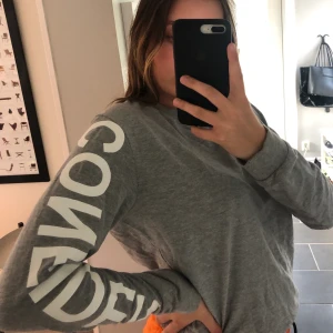 Grå sweatshirt - Text på armen: CONFIDENT Frakt tillkommer