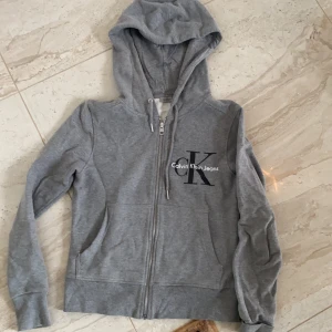 Calvin Klein hoddie jacka - I använt skick, ni ser fotot att fickan gått upp lite, vilket går att sy, o då syns det inte. Annars i gott skick.