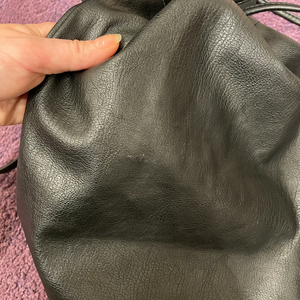 Svart ryggsäck från H&M. Skinnimitation. Storlek 30-10-32 cm.  På framsidan finns en repa som är nästan osynlig och små nötningar på snöret, som inte heller syns vid användning, annars fint skick. . Väskor.