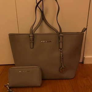 Michael Kors väska med plånbok - Äkta Michael Kors väska med tillbehörande plånbok i mycket bra skick som knappt är använd. I en ljusgrå matt färg med silvriga detaljer. Runt två år gammal och ordinarie pris är 2700kr. Plånboken kan köpa separat då för 300kr och väskan för 700kr