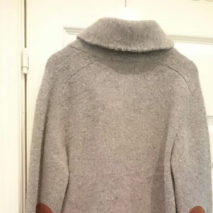  - Polo Ralph Lauren.  OANVÄND. Grå ullkofta med bruna mocka armbågslappar och bruna skinnknappar samt två fickor.                 - Köparen står för frakten -