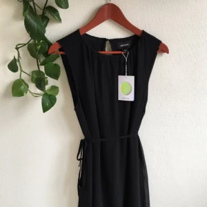  - Oanvänd långklänning från Monki. Knyts med tunt band i midjan. Underkjolen slutar strax under knähöjd. Övre tyglager är transparent svart tyg. Öppen något i ryggen.