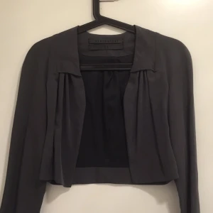  - Kort kavaj med fina detaljer från Minimarket. Mörkgrå färg i 100% tencel. Snygg till klänning! Perfekt till kontoret!