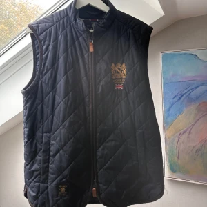 Blå quiltad väst från Morris - Mörkblå väst från Morris, i storleken small. Sömmarna har släppt i en av fickorna, därav blivit ett hål.