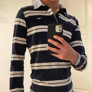 Randig pikétröja från Hampton Republic - Säljer en snygg randig pikétröja från Hampton Republic. Den är mörkblå med vita ränder och har en klassisk krage. Tröjan är knappt använd, då den inte är min stil. Stlk 170 men passar mig bra som är 177 cm.