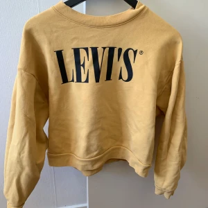 Gul sweatshirt från Levi's - Säljer en superfin gul sweatshirt från Levi's i storlek S. Den har en stor, svart Levi's-logga på framsidan och är perfekt för en avslappnad stil. Tröjan är i bra skick och gjord av mjukt material som är skönt att ha på sig. 