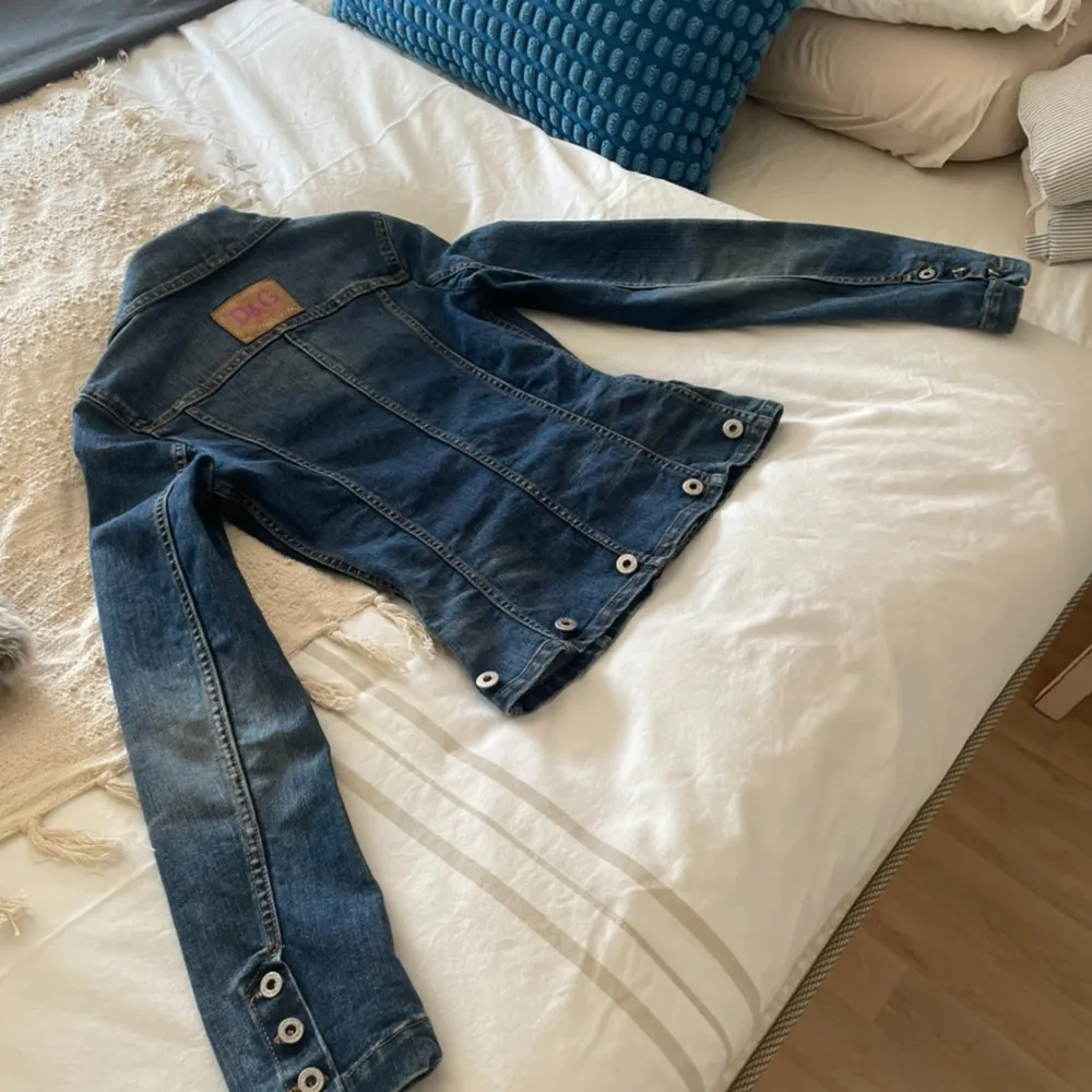 Säljer en snygg jeansjacka från D&G i klassisk blå denim. Jackan har en figursydd passform. Mått midja som bild 5, är 33 cm. Mått från armhåla till handled är 49 cm. Mått över byst 38cm. Står ingen storlek så XS är min gissning. . Takit.