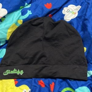 Svart mössa med broderad text - Säljer en svart sixties mössa med en cool broderad text i grönt. Perfekt för att hålla sig varm och stilren under kyliga dagar. Passar till alla outfits!