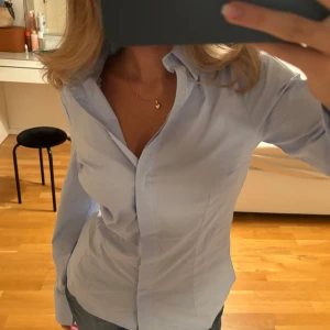 Blå skjorta - Säljer denna virala skjortan som är helt ny😍😍 figurnära och går in i midjan, formar kroppen så så snyggt!!! Storlek xs men passar xs-s💕💕 älskar att knapparna är ”osynliga” och att man kan ha den lite offshoulder om man knäpper upp