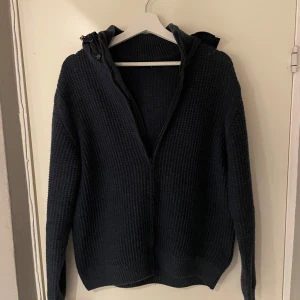 Mörkblå stickad hoodie från Polo Club - Säljer en snygg och bekväm mörkblå stickad hoodie/cardigan från Polo Club. Perfekt för kyliga dagar med sin mysiga huva och dragkedja framtill. Tröjan har långa ärmar och en ribbad struktur som ger en stilren look.