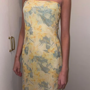 Blommig axelbandslös klänning som kan användas som långkjol! - Snygg axelbandslös klänning med blommigt mönster i ljusgult och grönt. Perfekt för sommarens festligheter. Klänningen har en smickrande passform och är i en lång modell.