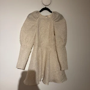 Vit klänning med puffärmar - Elegant vit klänning med lång puffärm och strukturmönster. Klänningen har en dragkedja i ryggen och en rund halsringning. Perfekt för speciella tillfällen. Perfekta STUDENT klänningen, säljer då jag köpte den i två stolekar köpt secondhand men finns inga täcken på användning! Skriv för mer bilder 💛den är vit/creamfärgad