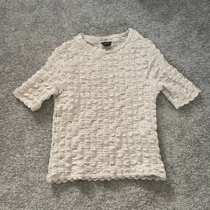 Beige topp från Lindex - Säljer en beige topp från Lindex med ett unikt texturerat mönster. Toppen har korta ärmar och en rund halsringning. Köpt för 200kr, använd ungefär 2-4 gånger💘