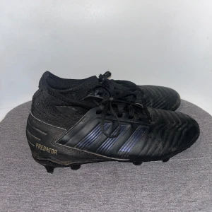 Svarta Adidas Predator fotbollsskor - Säljer ett par svarta Adidas Predator fotbollsskor med snörning och dubbar. Skorna har en stilren design med diskreta ränder och är perfekta för fotbollsplanen. Skon har en strumpa och är väldigt behagliga att ha på sig☺️✨pris går att diskutera