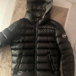 Svart dunjacka från Colmar - Säljer en svart dunjacka från Colmar med huva och dragkedja. Jackan är använd, men är i fint skick. Storlek 44 enligt deras hemsida, men det motsvarar 34/xs. Har fler bilder med jackan på så de är bara att skriva att fråga!❤️