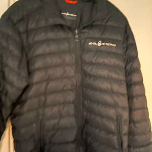 Svart pufferjacka från Sail Racing - Snygg svart pufferjacka från Sail Racing med dragkedja framtill. Jackan har en quiltad design och är perfekt för kyligare väder. Den har långa ärmar och en stilren look.