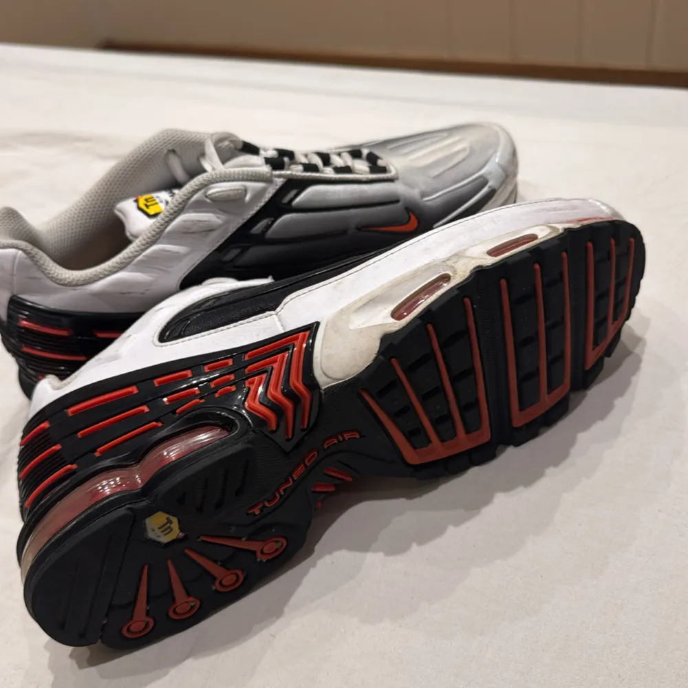 Snygga Nike Air Max sneakers i silver med svarta och röda detaljer. Skorna har en futuristisk design med synlig dämpning i sulan och klassisk snörning. Perfekta för en sportig look.. Kengät.