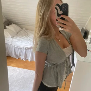 Grå kortärmad bolerotopp - Snygg grå bolerotopp med korta ärmar och knytning framtill. Perfekt för lager-på-lager-stil och passar till många olika outfits.