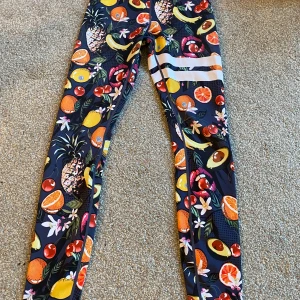 Färgglada leggings med fruktmönster - Snygga och färgglada leggings med ett livligt fruktmönster. Perfekta för att liva upp din garderob med ananas, apelsiner, bananer och avokado. De har en tight passform och är gjorda i ett stretchigt material för extra komfort. Från stronger