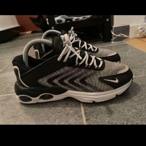 Svart och grå Nike sneakers - Snygga Nike sneakers i svart och grått med vit sula och snörning. Skorna har en sportig design med tydlig Nike-logga på sidan och tå. Perfekta för en aktiv livsstil.