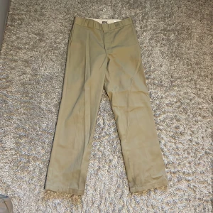 Beige byxor från Dickies 874 - Snygga beige byxor från Dickies med rak passform. Perfekta för en avslappnad stil. Byxorna har en klassisk design med fickor och en diskret logga baktill.