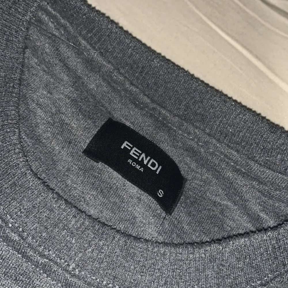 Säljer en grå tröja från Fendi med coola gula ögon på bröstet. Tröjan har långa ärmar och är perfekt för en avslappnad stil. Passar bra till både jeans och sneakers.. Neuletakit & Villapaidat.